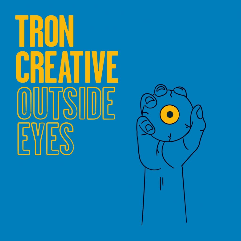 Outside Eyes promotional visual. Text reading Tron Creative Outside Eyes with a hand holding an eyeball with a yellow iris against a blue background.