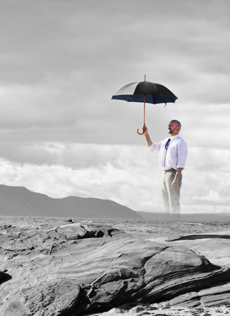 Love Beyond (Act of Rembrance) promotional image.A man holding a large black umbrella and whose legs seems to disappear into nothing hovers over a coastal landscape. He is staring into the distance.